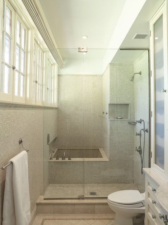 paredes revestidas de mosaicos en tonos beige, ducha y bañera con mampara