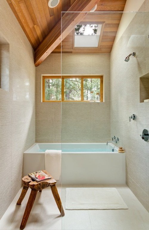bañera y ducha juntas, con mampara transparente, techos de madera y paredes de cerámicos beige