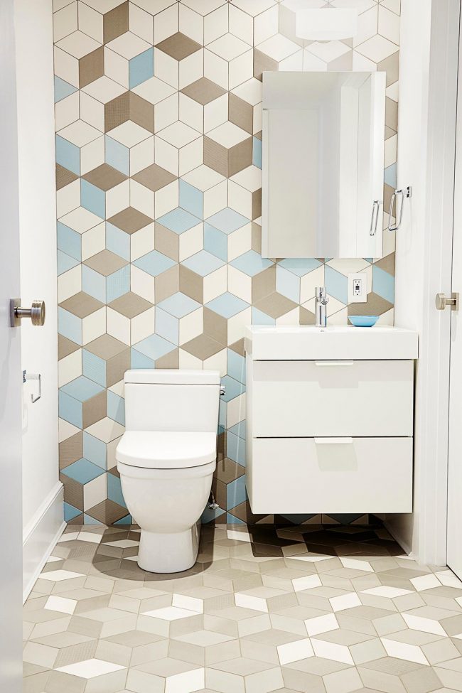 pared con azulejos hexagonales en blanco, celeste y blanco que simulan cubos, inodoro y mueble bajo blancos
