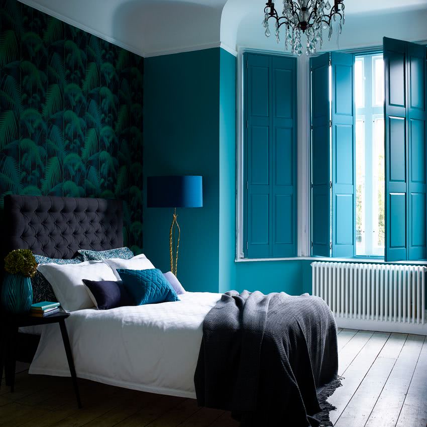 paredes azul intenso, empapelado con vegetación, cama en gris oscuro y blanco, cojines en tonos de azul