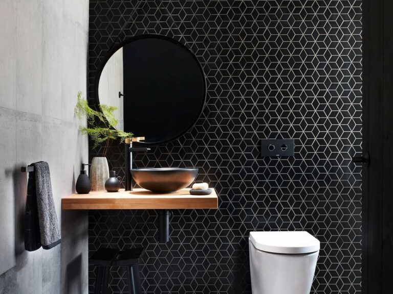 baño con pared con azulejos negros hexagonales, encimera en madera, inodoro blanco