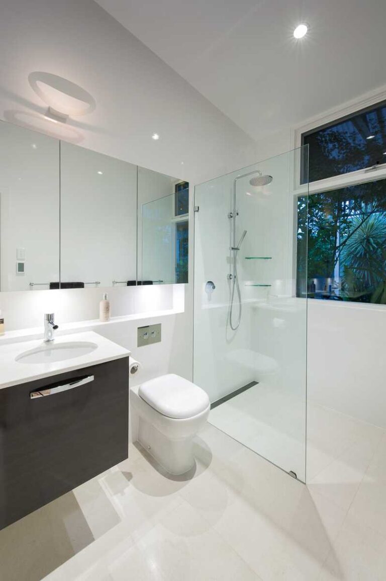 baño moderno con paredes y suelo blancos, ducha con mampara
